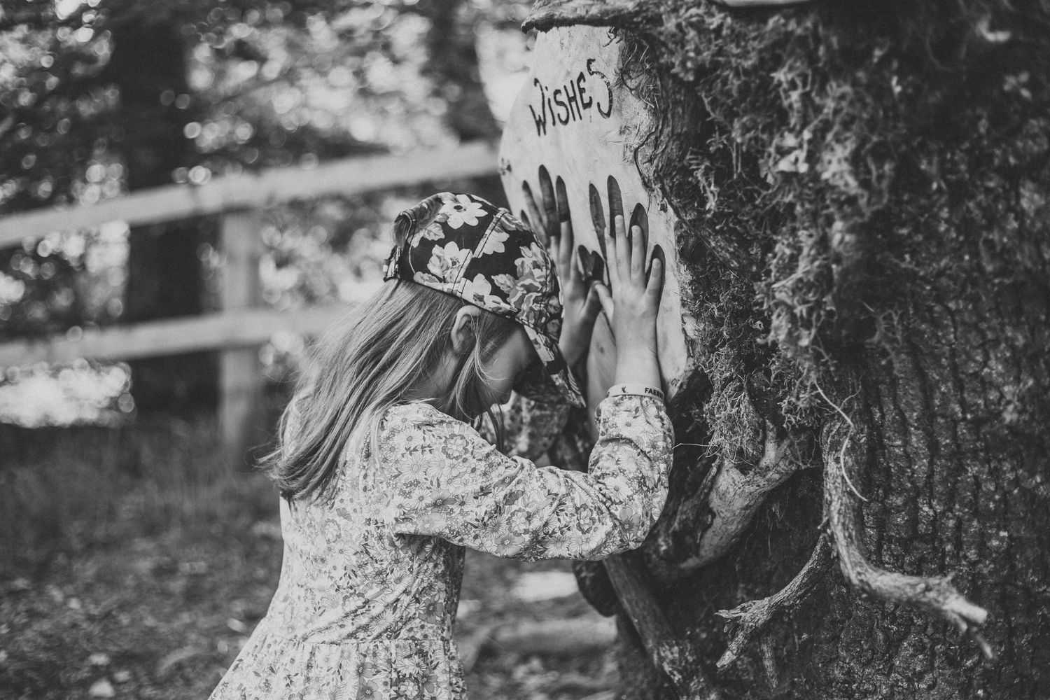 A person in a floral dress examining markings on a tree trunk in black and white photography.