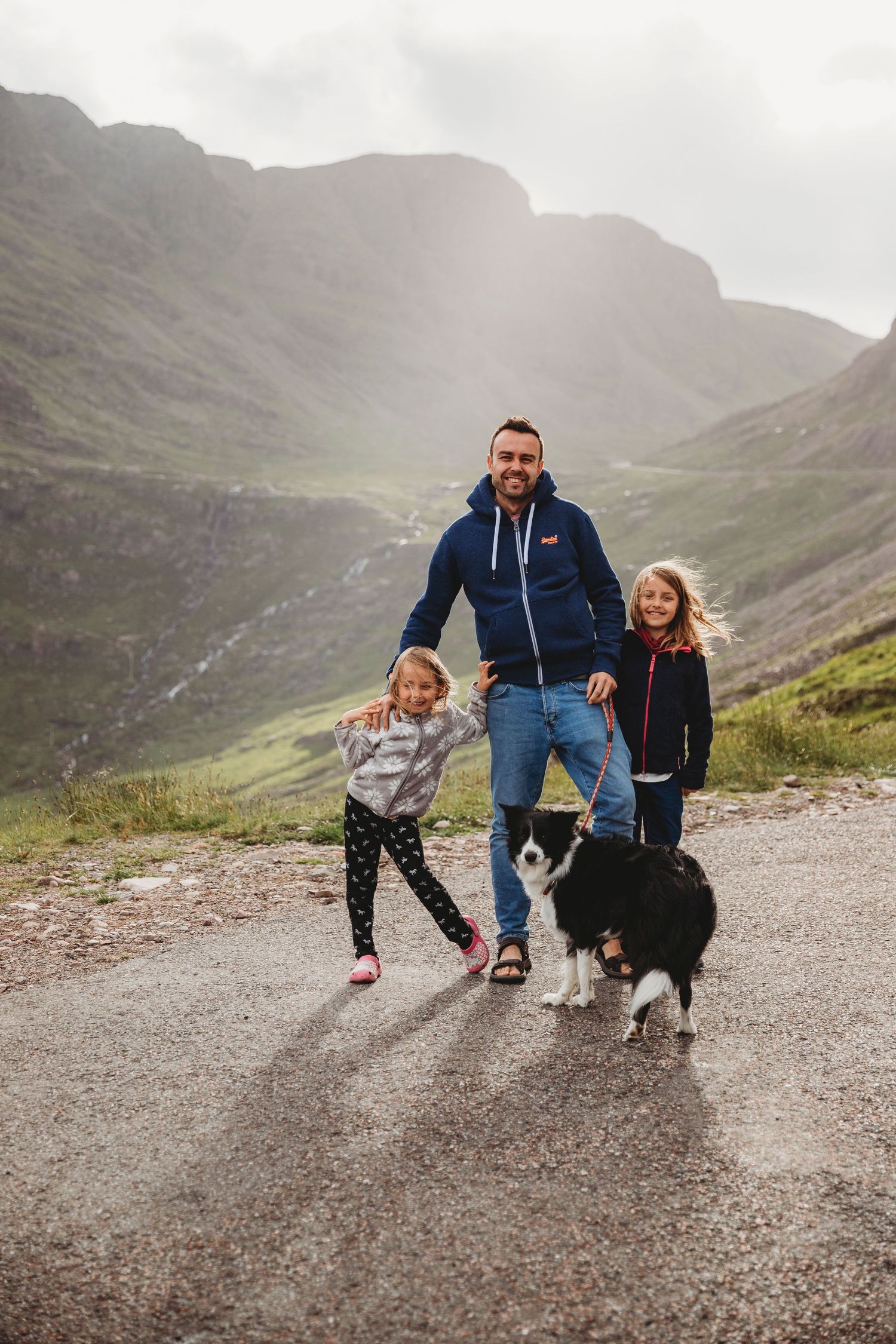 A family and their Border Collie enjoy a hike together on a misty mountain trail in Scotland.