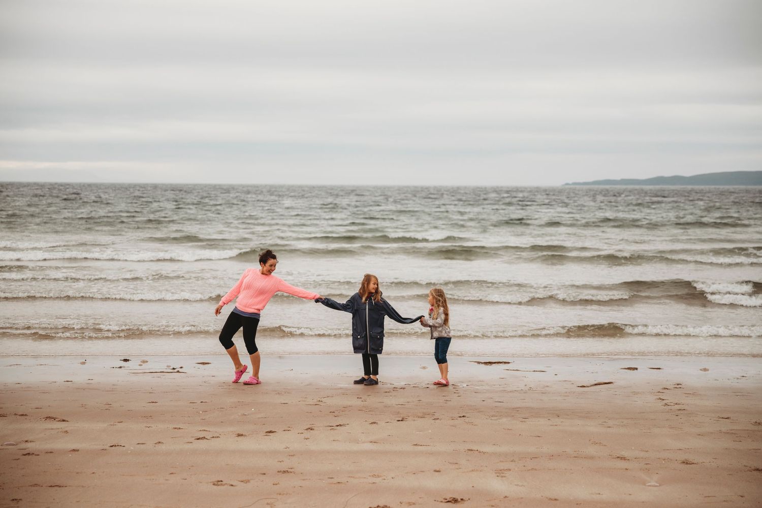 People playing and holding hands on a windswept beach.