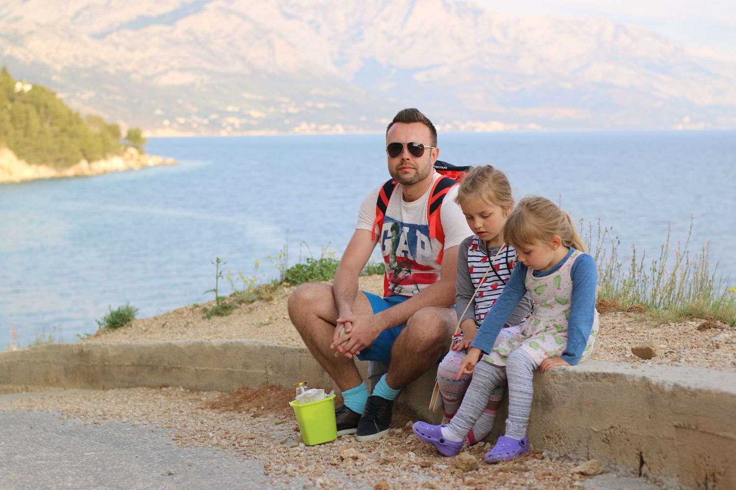 Family takes a break on a scenic coastal overlook with mountains and sea in the background.