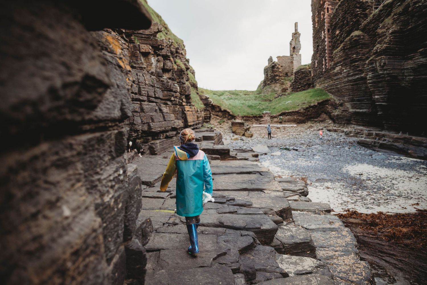 Person in blue raincoat walking along dramatic coastal rock formations.