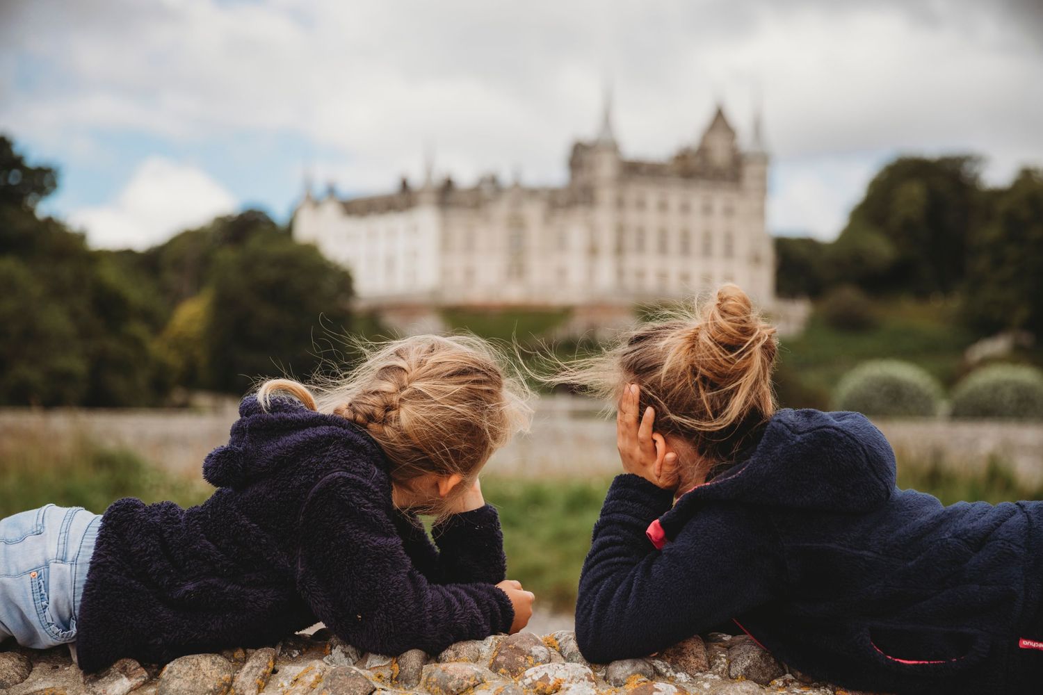 Two figures lying on grass viewing a majestic castle on a hill in Scotland.