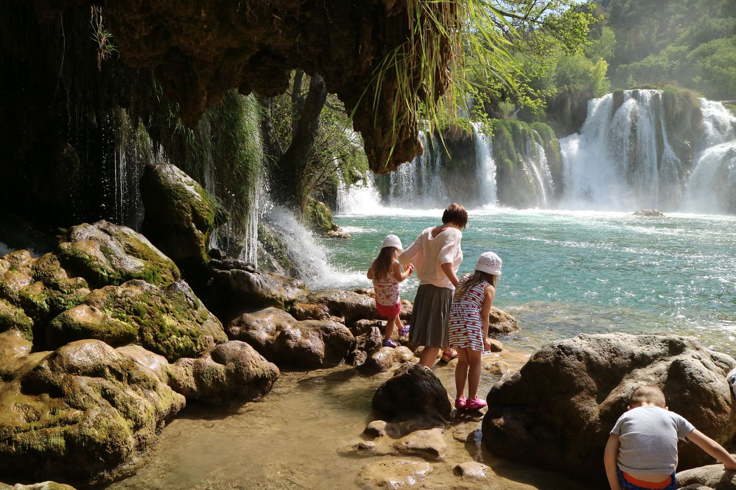 Visitors explore a scenic waterfall grotto with multiple cascading waterfalls and rocky terrain.