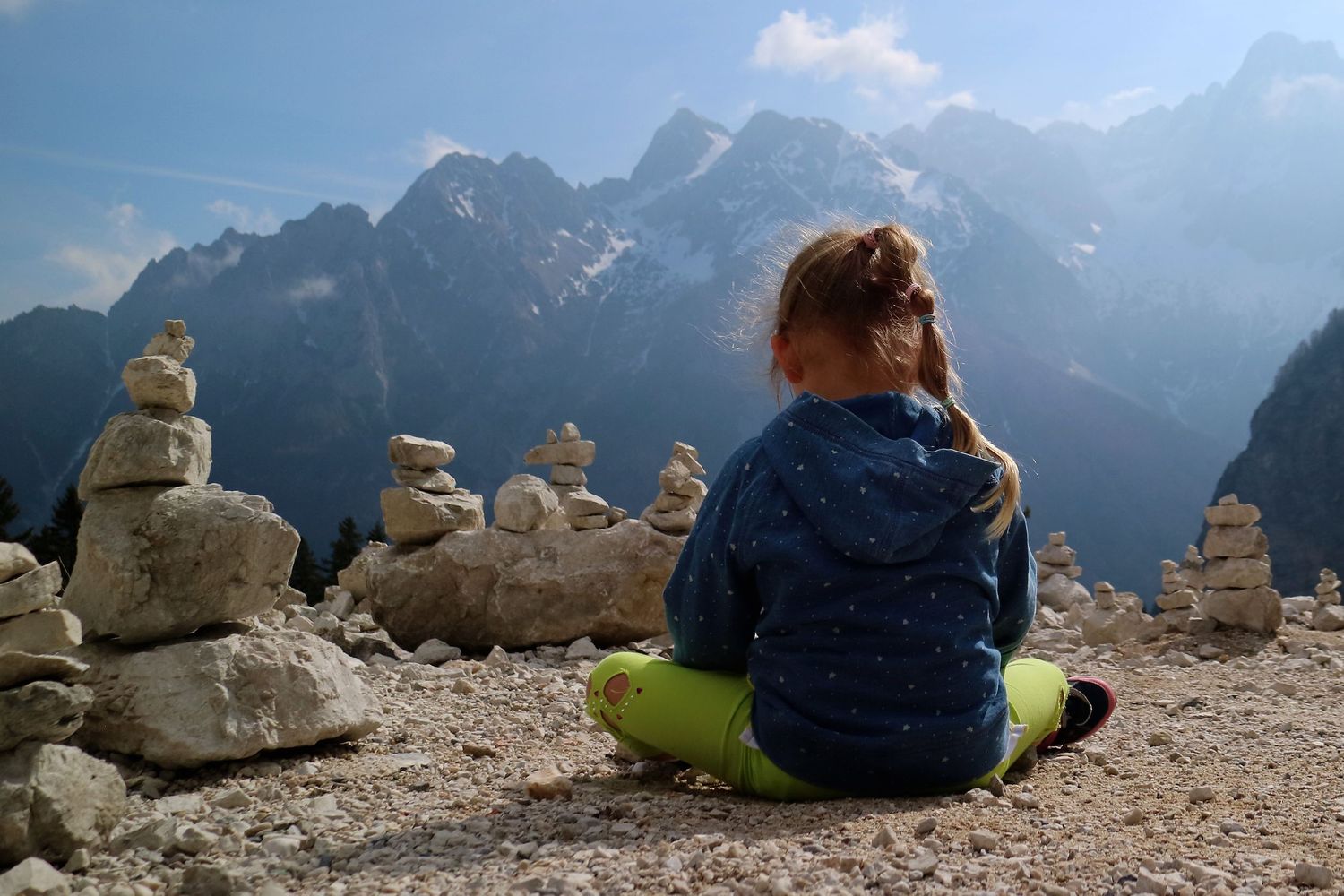 Person sitting among stone cairns overlooking dramatic mountain peaks.