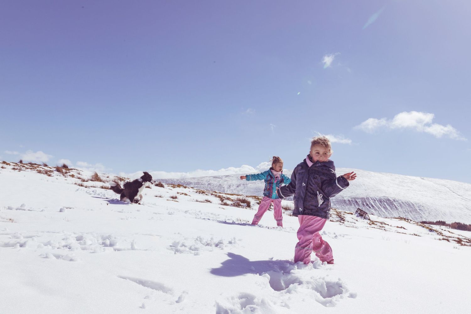 Children playing in the snow on a sunny winter day with mountains in the background.