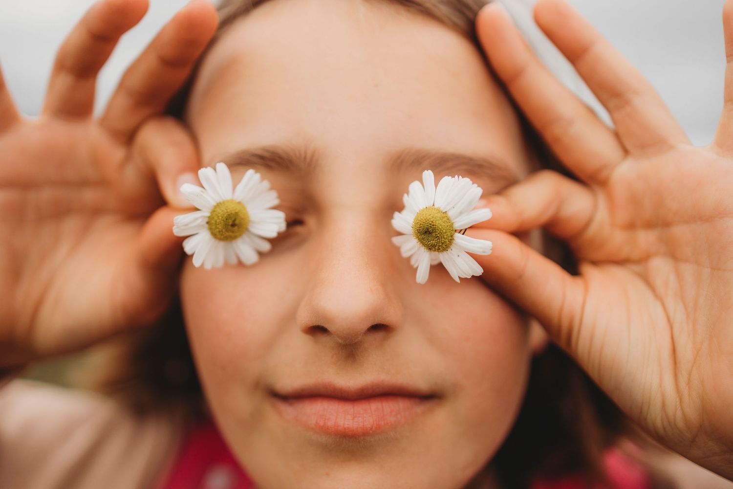 A creative portrait showing daisies placed over closed eyes with a gentle smile.