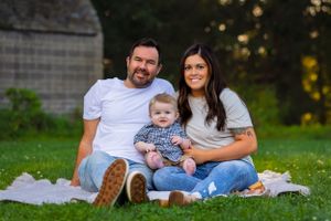 A young mom and dad sit with their baby, cozied up on a blanket enjoying each other's company