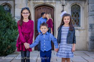 three children hold hands while their parents stand behind them stealing a kiss in the background