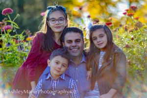 a father sits among a field of flowers with his children. sun streams behind them