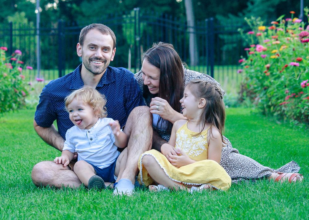 a family with young children sit outside in the grass and laugh at each other