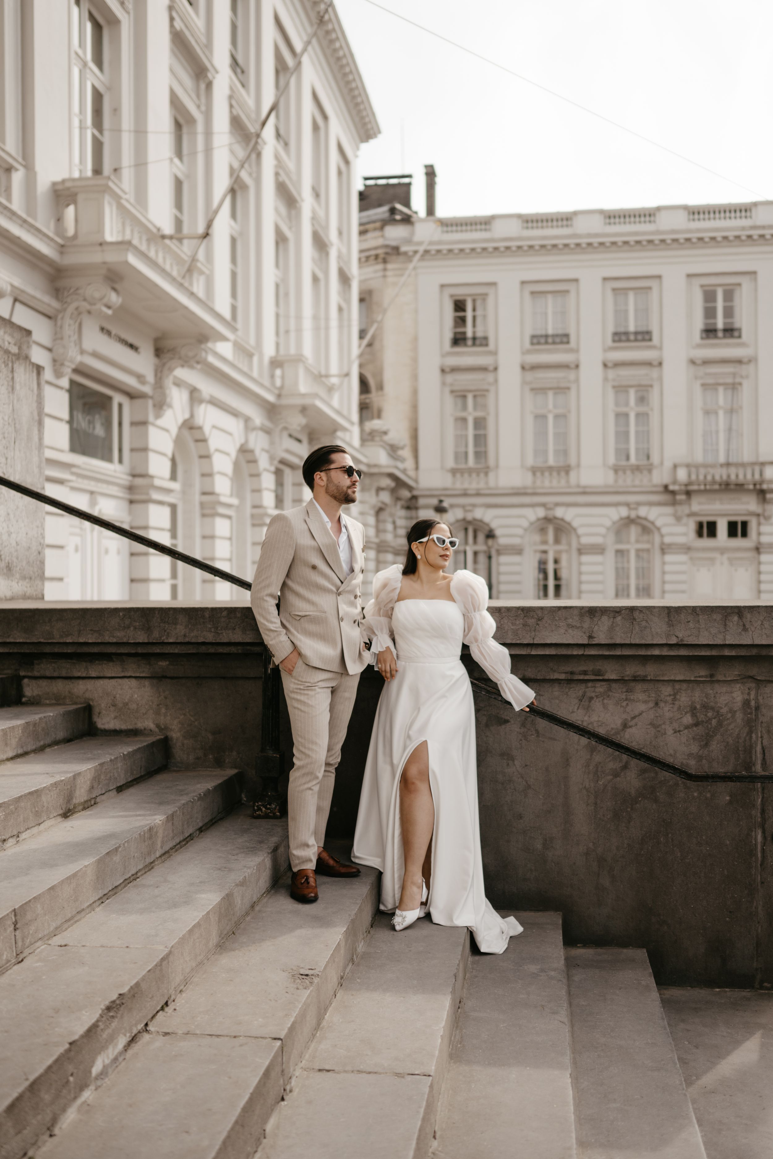 Elegant wedding couple poses on grand stone steps of historic building in formal attire.