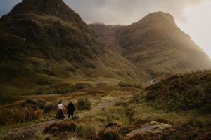 Misty mountains rise dramatically in the Scottish Highlands as hikers traverse the rugged terrain.