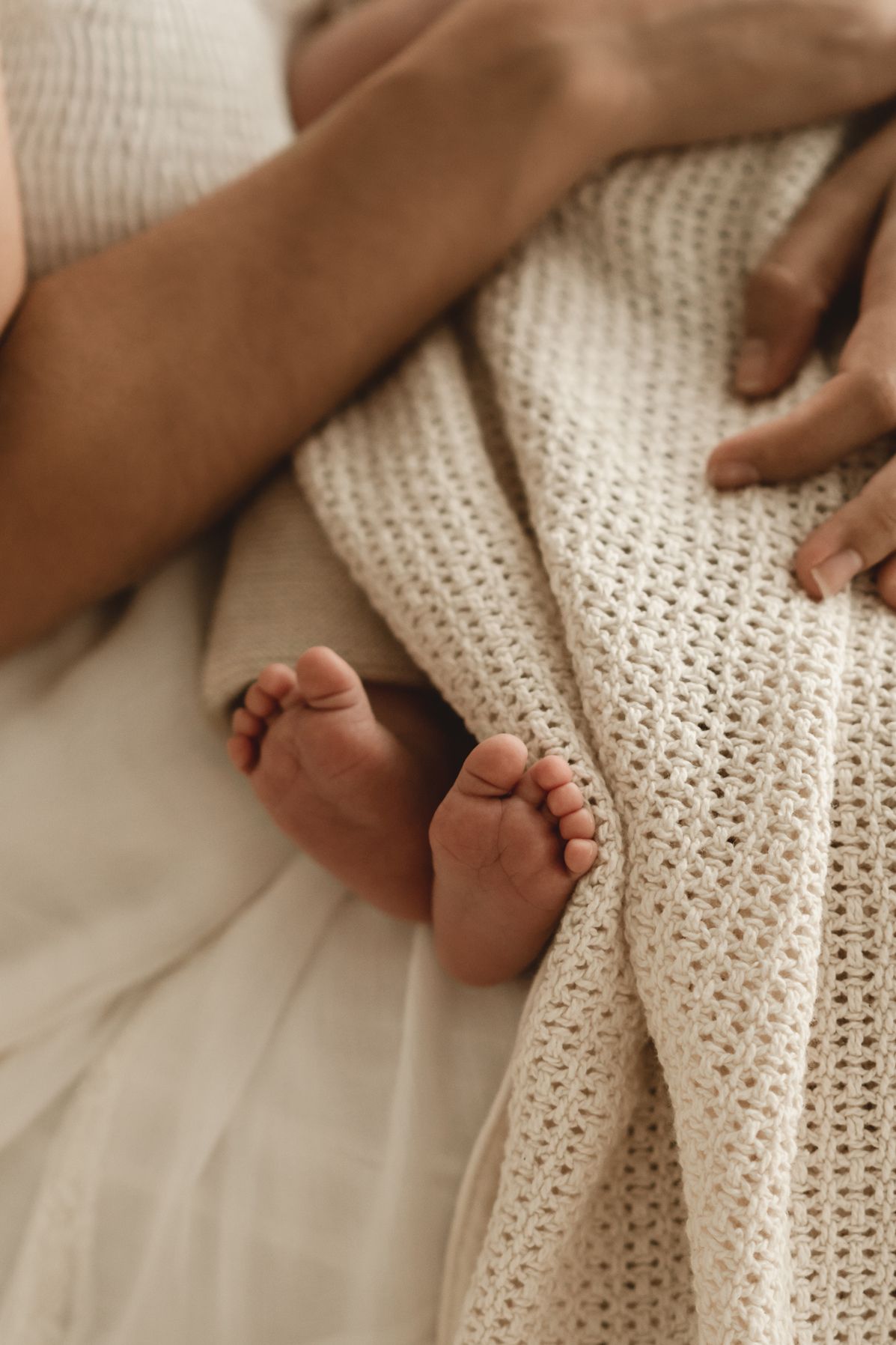 Close up of tiny baby feet peeking out from soft knitted blanket.