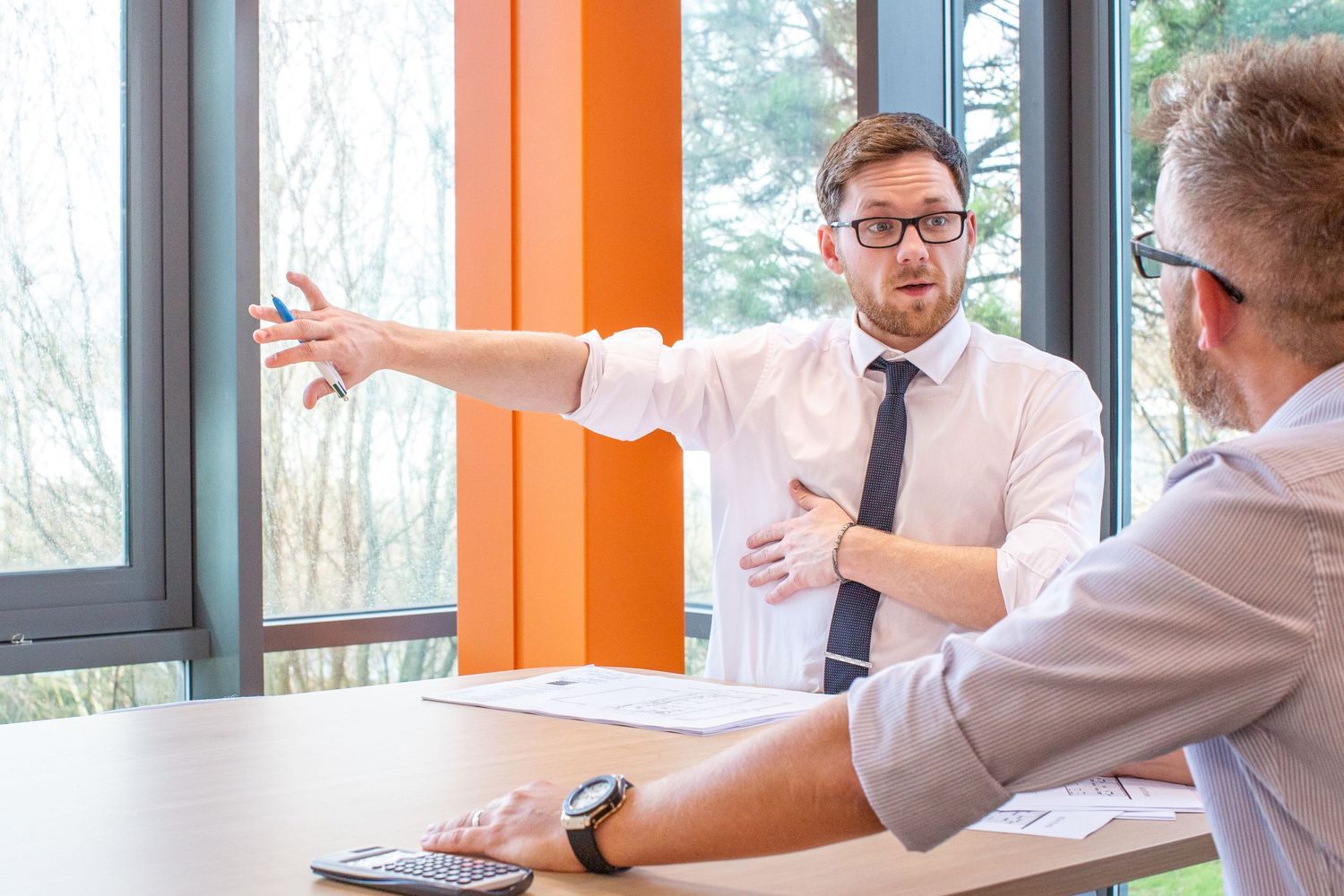 Two professionals having an animated discussion in a modern office with orange walls.