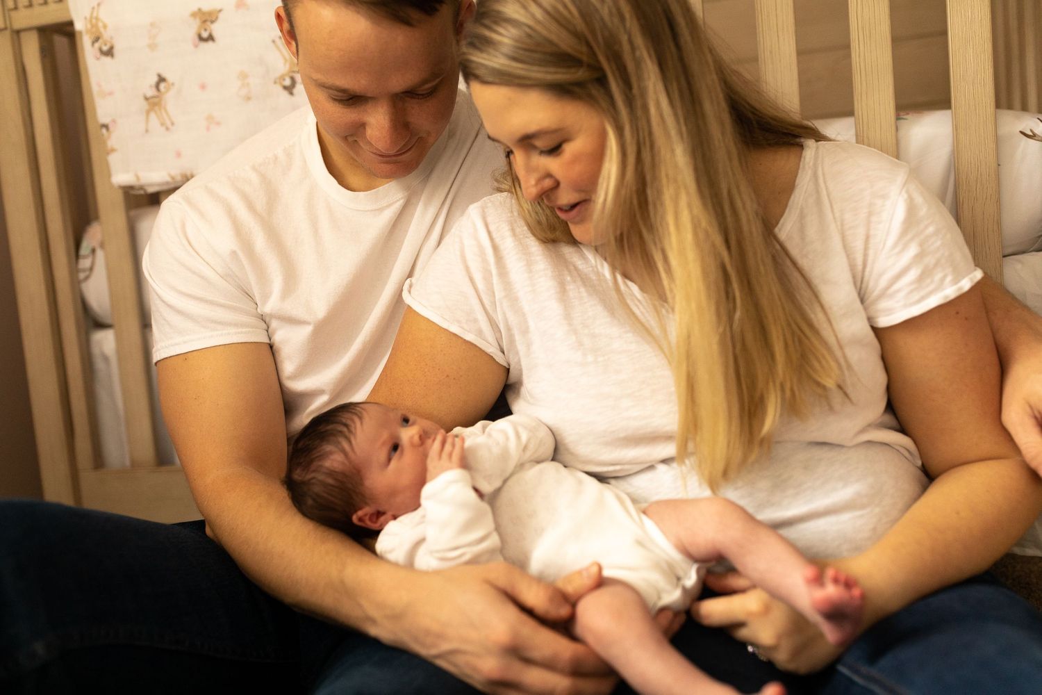 An intimate family portrait in warm lighting as they cuddle their newborn by the crib.