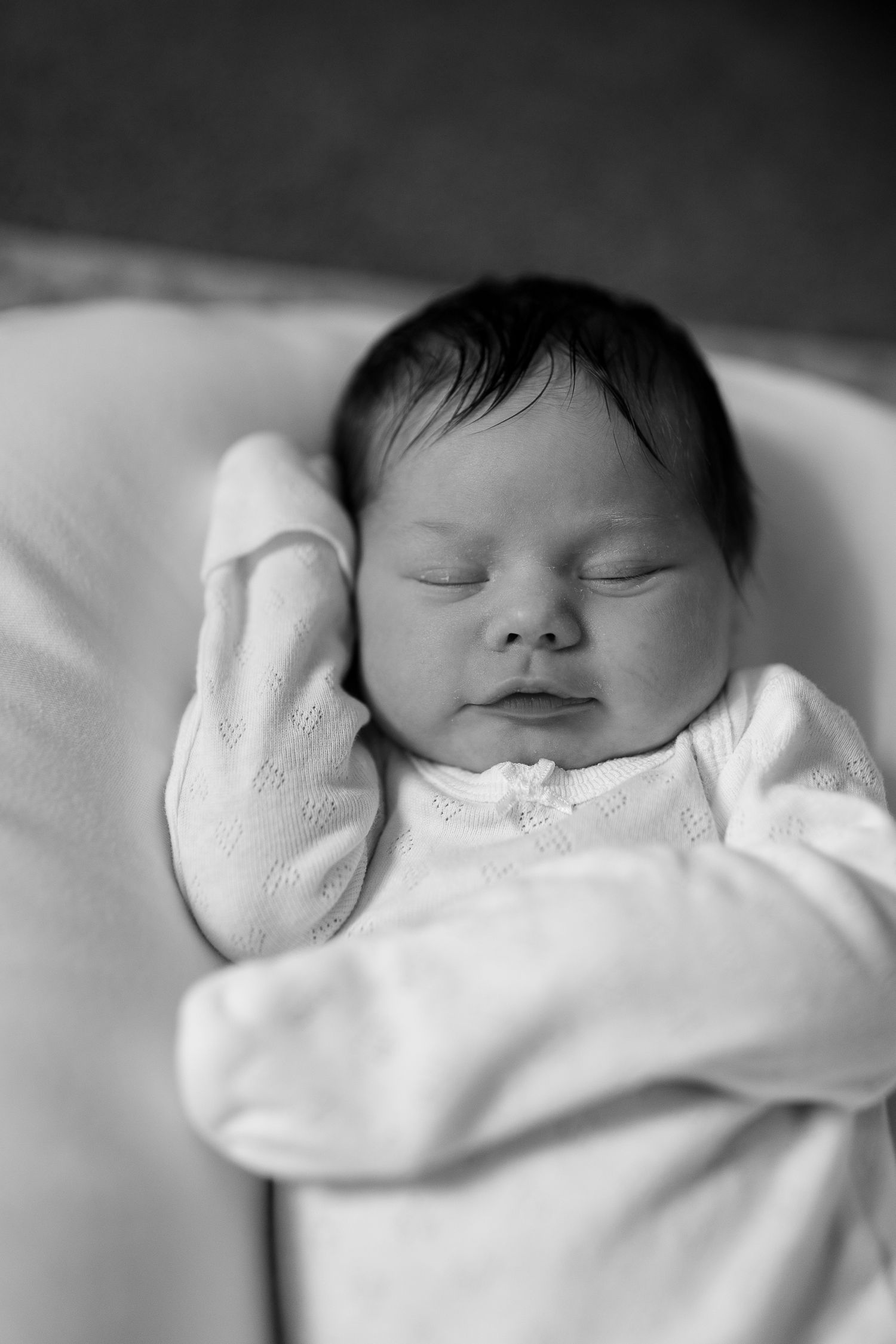 A peaceful black and white portrait of a sleeping infant in white clothing.
