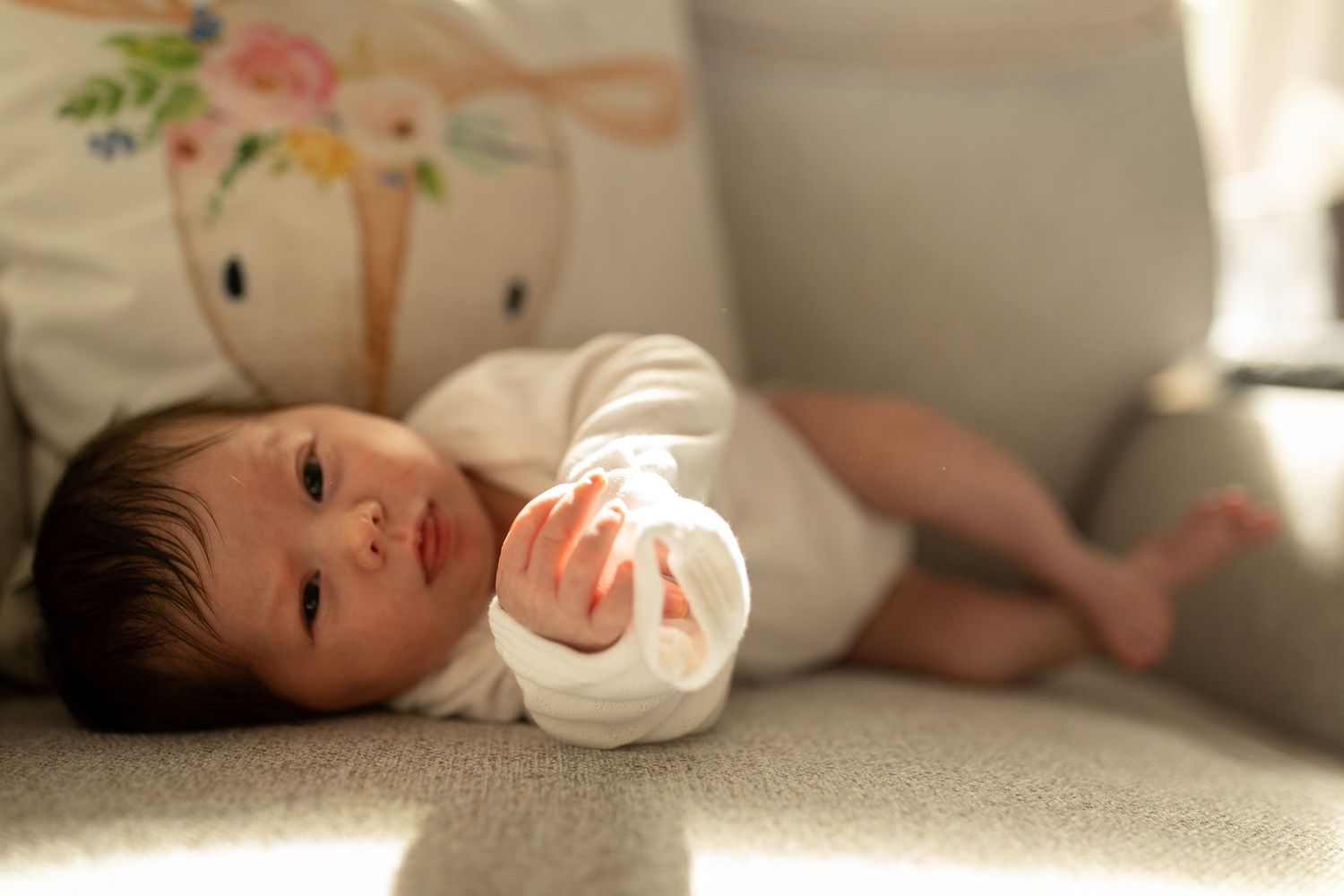 Baby in white clothing with decorative badge rests in warm lighting.