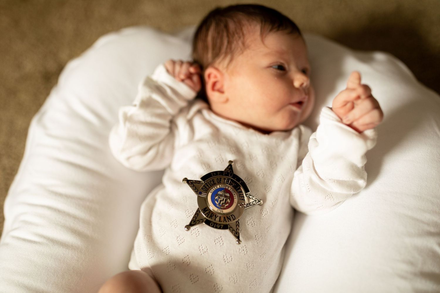 Baby in white clothing with badge detail stretches on white cushioning.