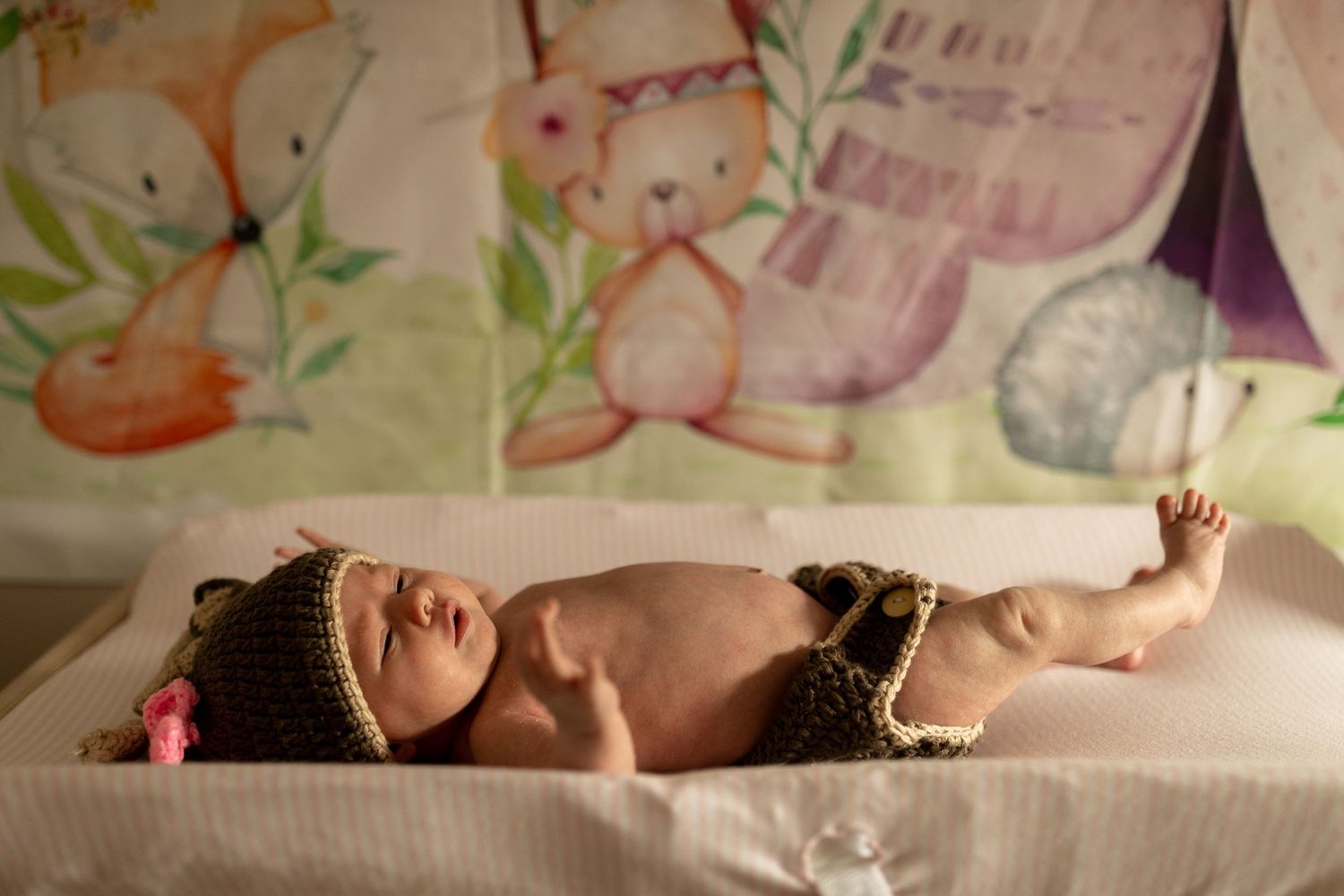 Newborn baby lying on white blanket wearing brown knitted accessories.