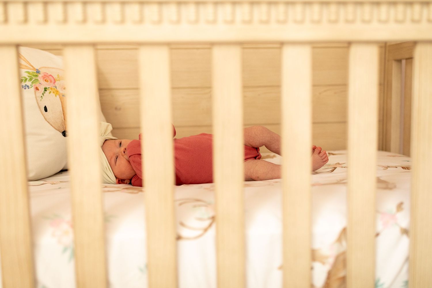 View through white crib slats of sleeping baby in nursery.