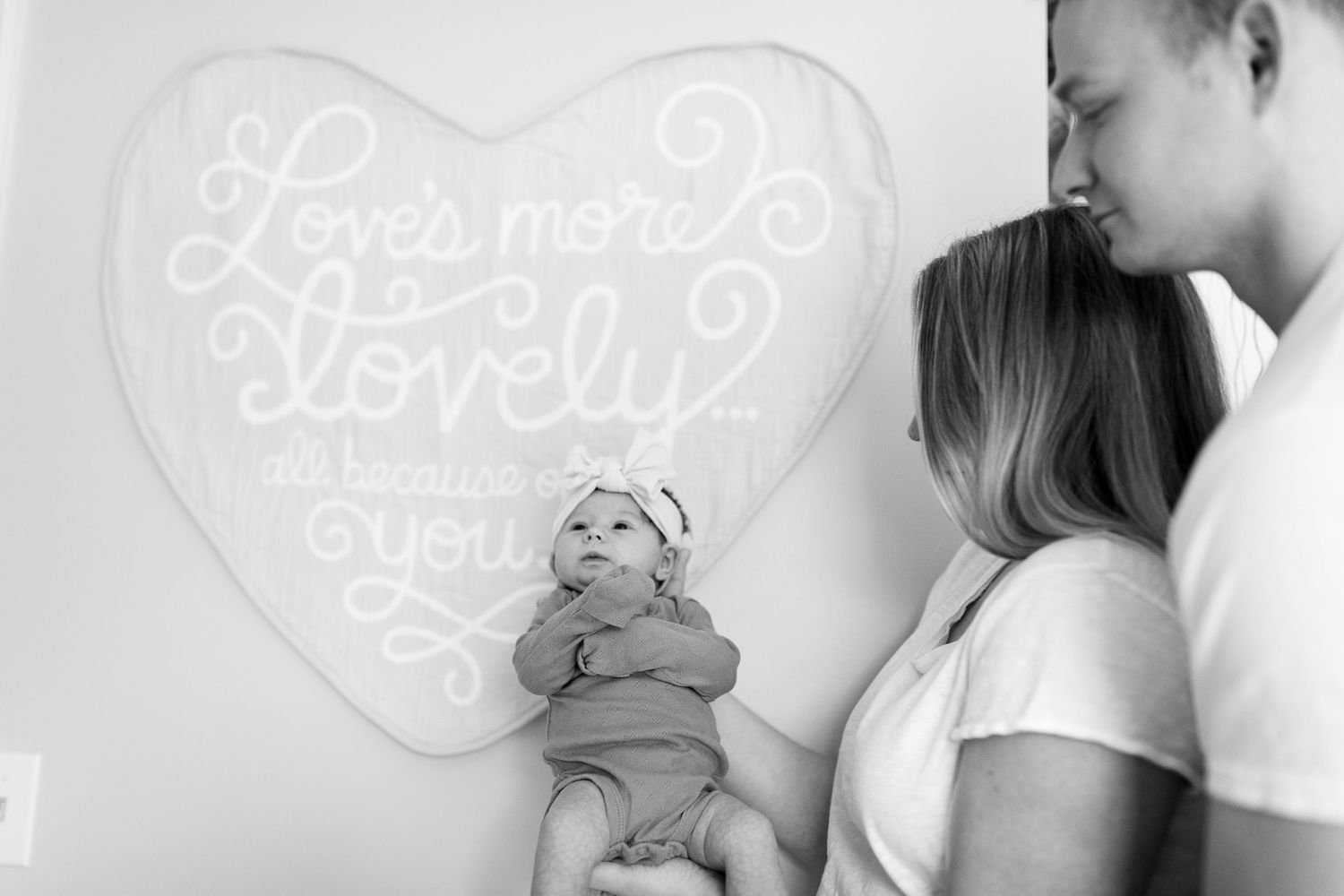 Black and white photo of couple with baby near heart wall decor.