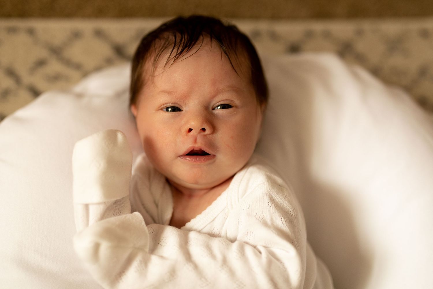 A peaceful newborn rests in soft white clothing against plush bedding.