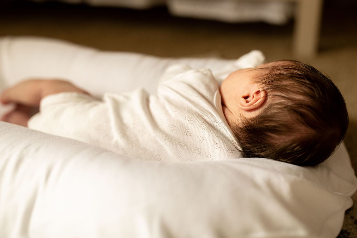 Baby in white clothing sleeping on soft white bedding in natural light.