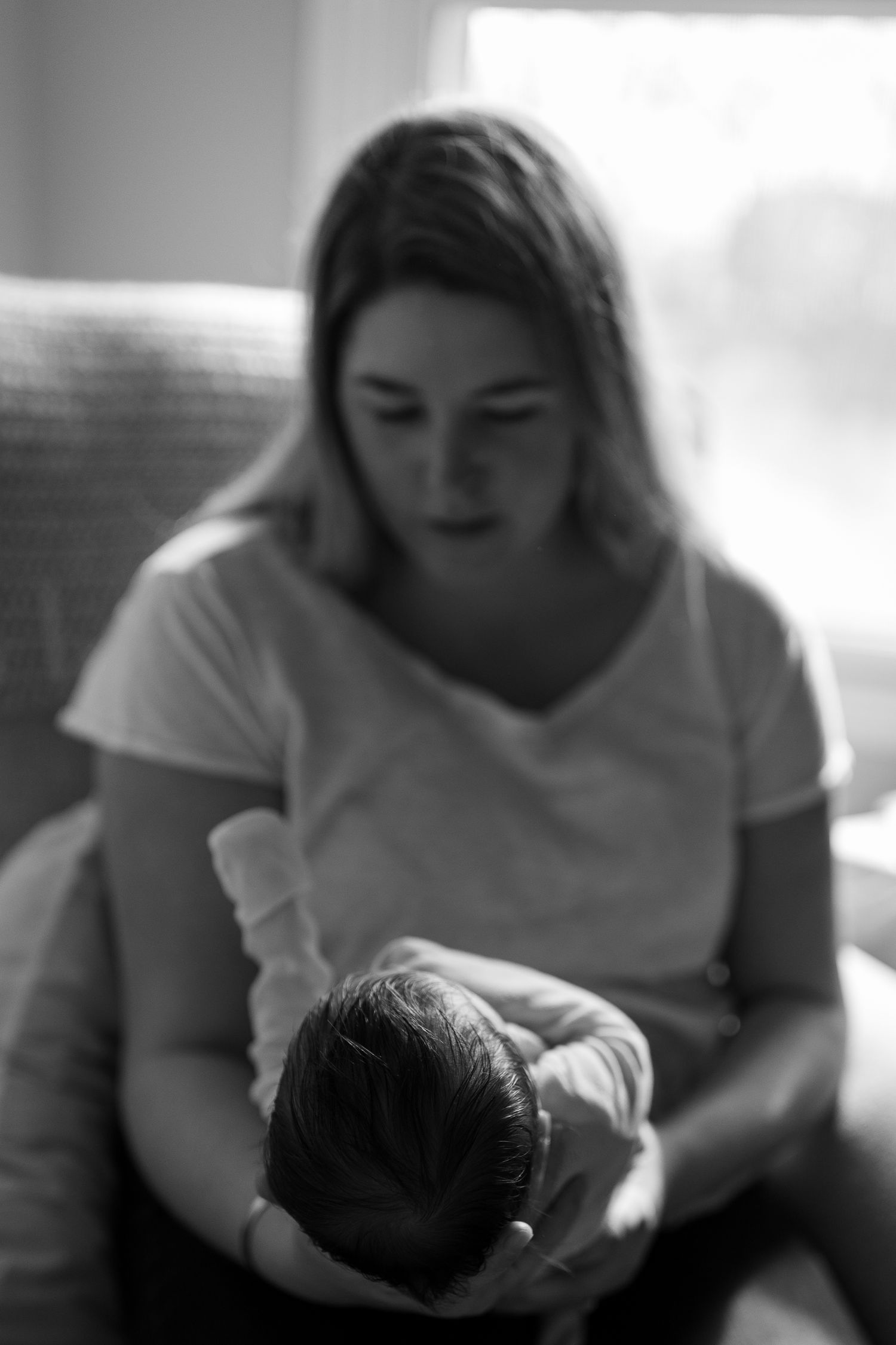 Black and white images of mother cradling newborn baby in gentle natural lighting.