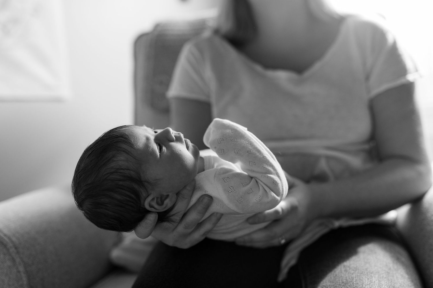 Mother holding sleeping newborn baby in gentle monochrome lighting.