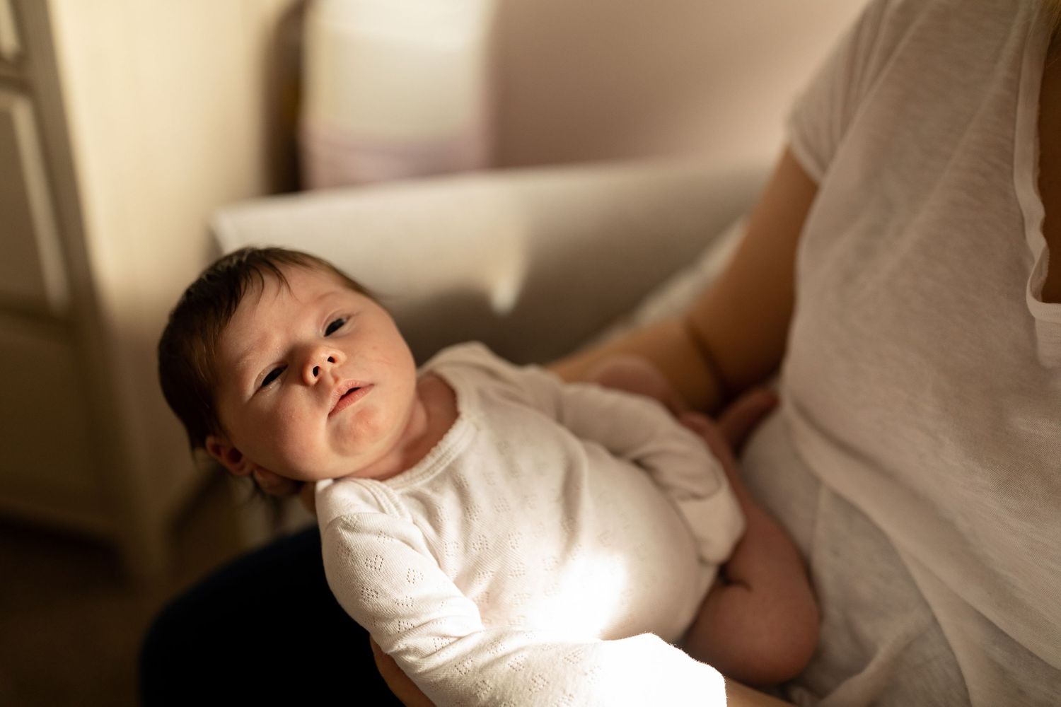 Newborn baby resting on white bedding in natural sunlight.