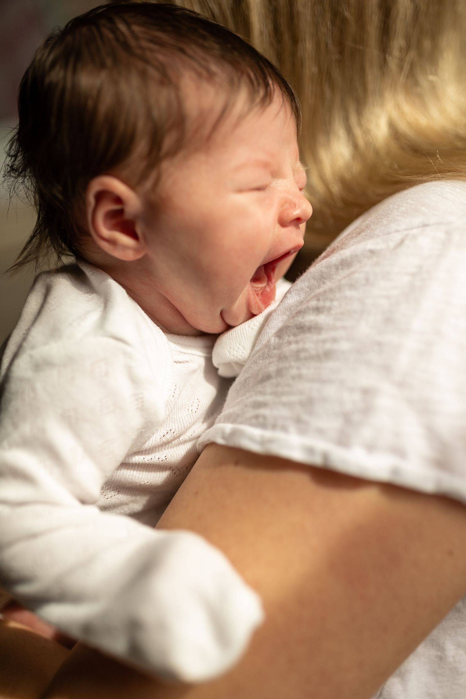 Baby in white clothing sleeping peacefully against soft textured background.