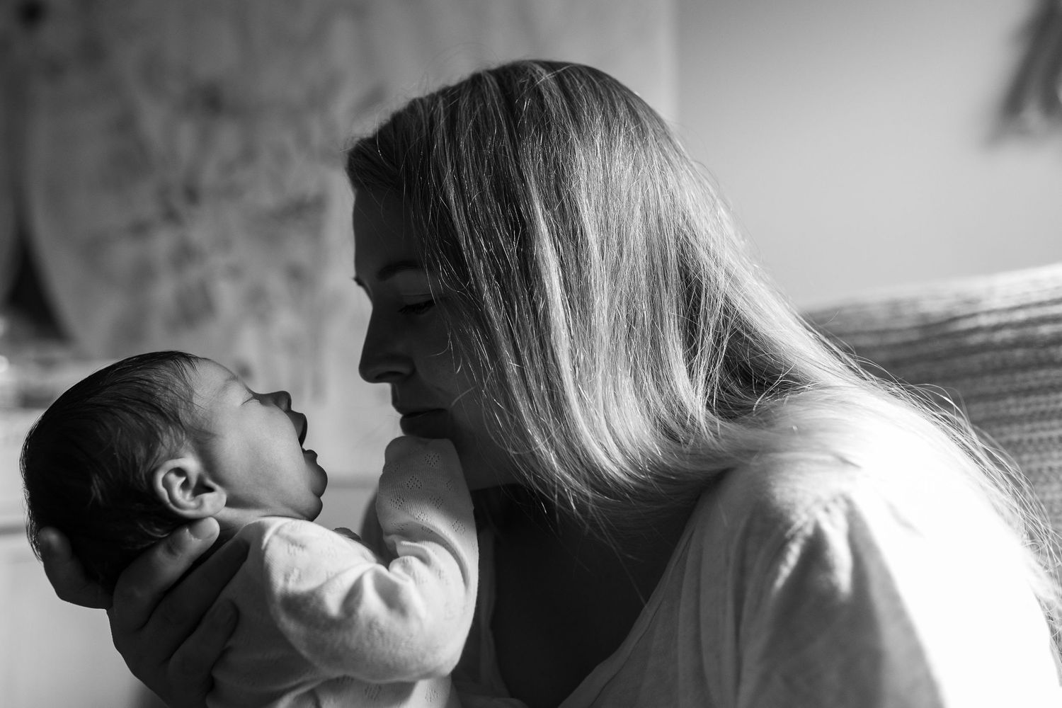 A tender black and white moment between a parent and newborn baby against a light background.