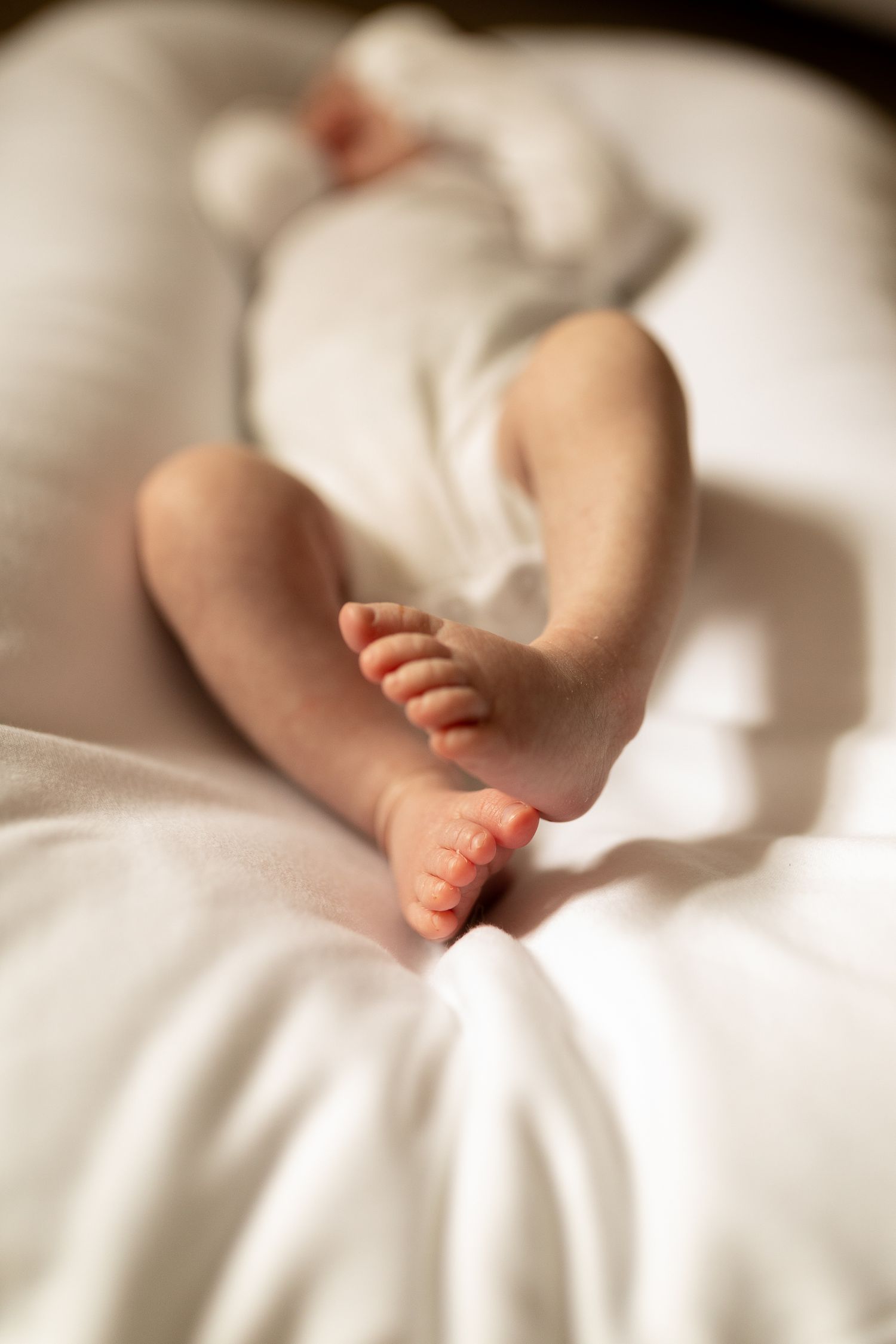 Close-up of tiny baby feet against white bedding in natural light.