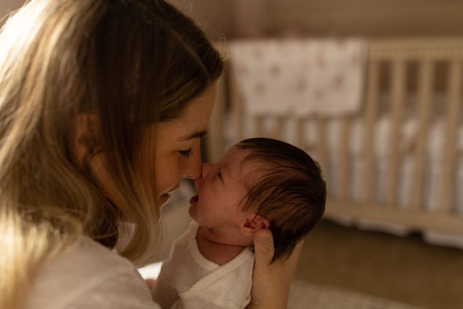 Intimate bonding moment between parent and newborn in nursery with crib in background.