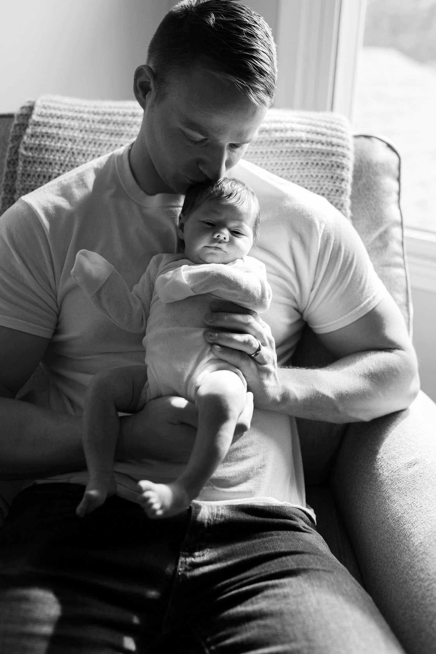 Parent in white t-shirt tenderly holding sleeping newborn baby in black and white portrait.