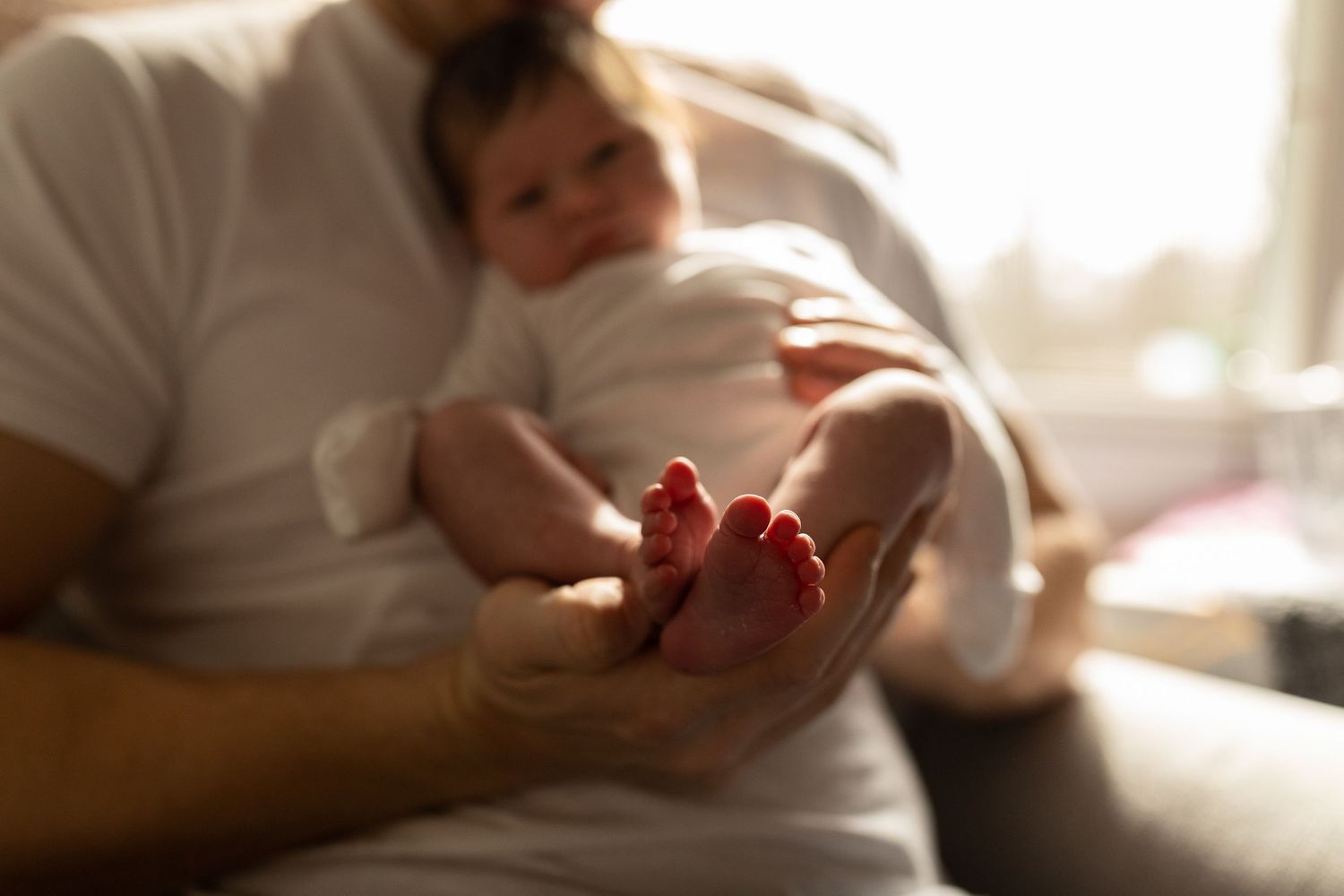 Close-up of tiny baby feet being held by caring hands in warm lighting.