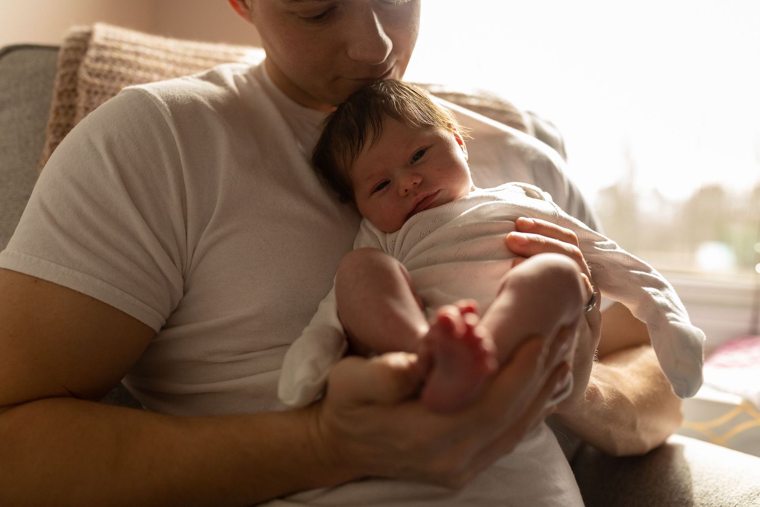 Parent in white shirt gently holding and examining newborn in warm natural light.