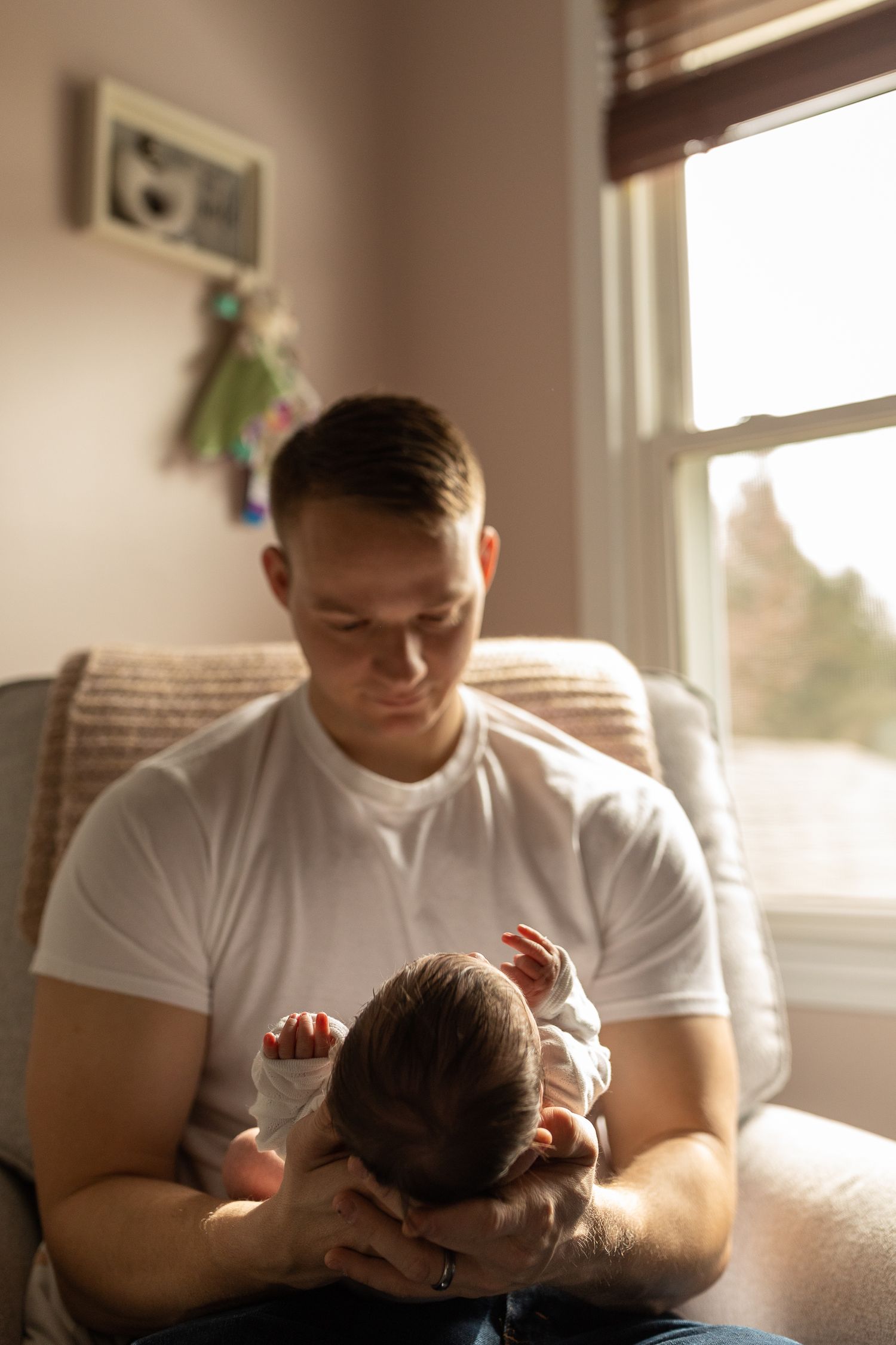 Parent and baby sharing quiet moment in sunlit room near window.