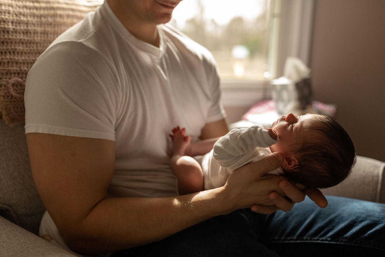 Parent in white t-shirt tenderly holding newborn in afternoon sunlight.