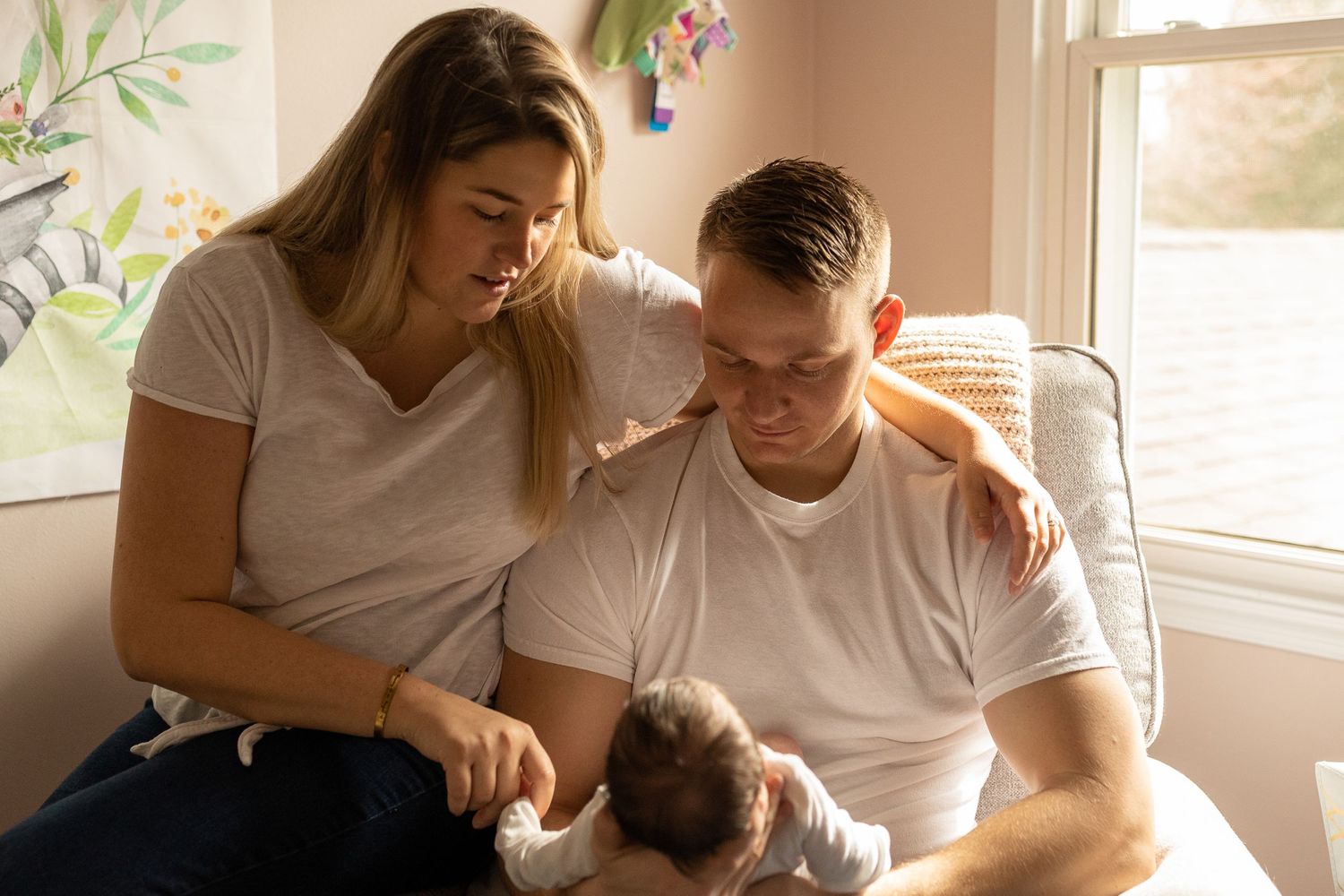 Family sharing intimate moment with newborn baby by sunlit window.
