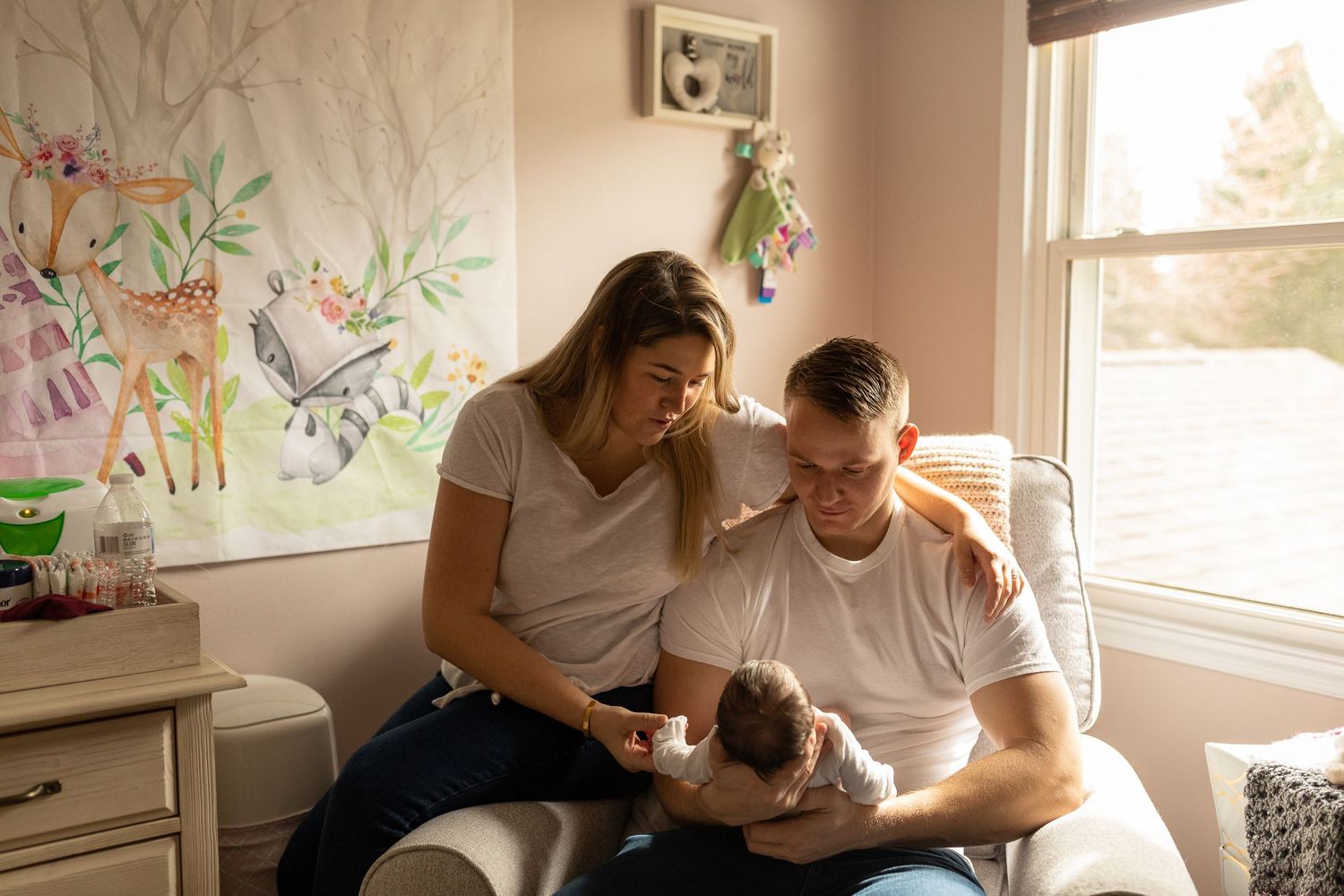 A peaceful nursery scene with floral wallpaper as parents tend to their newborn near a window.