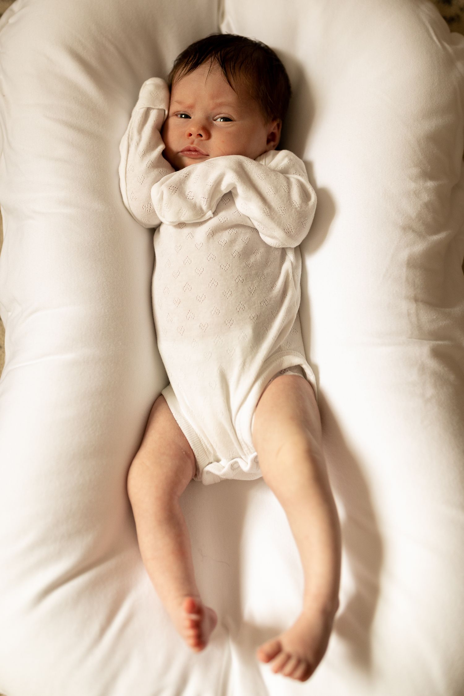 A resting infant in white onesie on plush white cushioning.