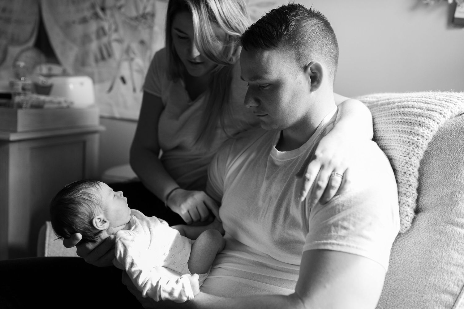 A tender black and white moment showing a newborn being cradled and watched over in a quiet room.
