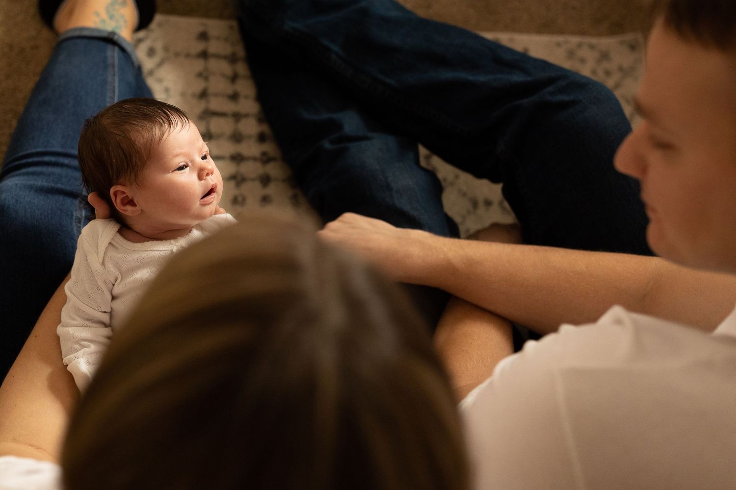 A small baby laying on blue fabric while being gently interacted with by adults.