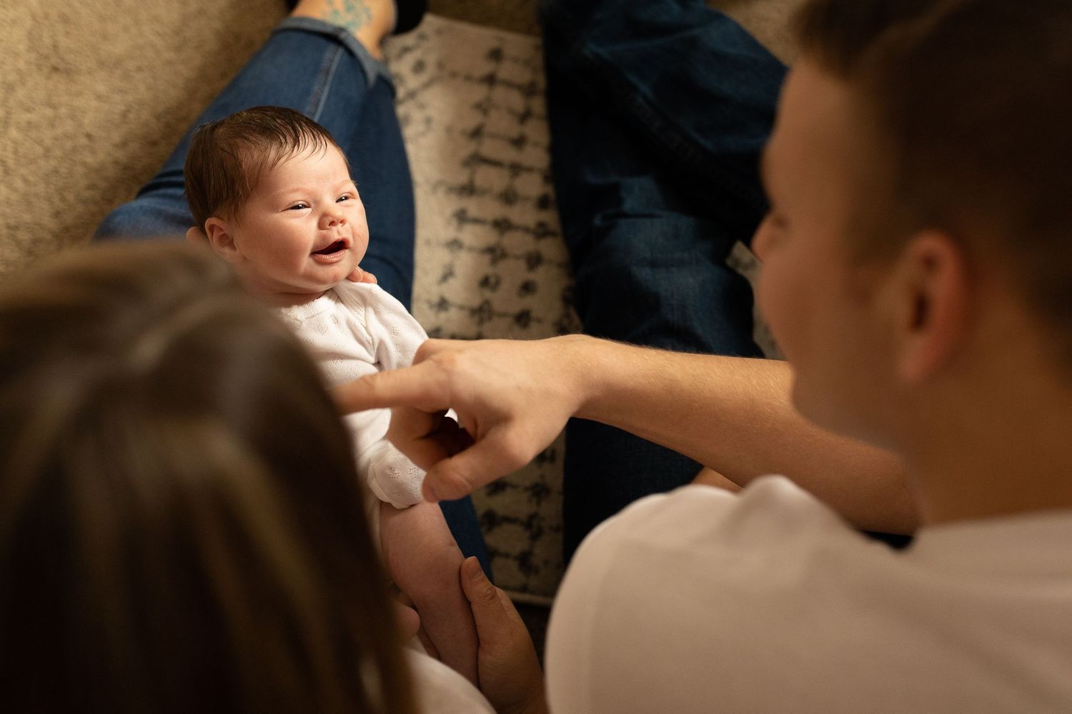A newborn baby in white clothing expresses emotion while being attended to on blue fabric.