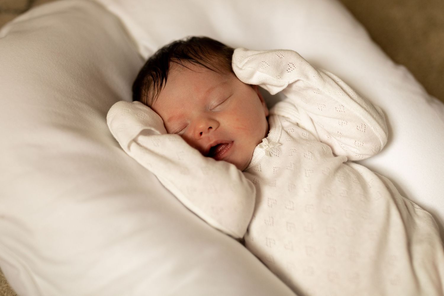 A sleeping infant in white clothing nestled in cozy white bedding.