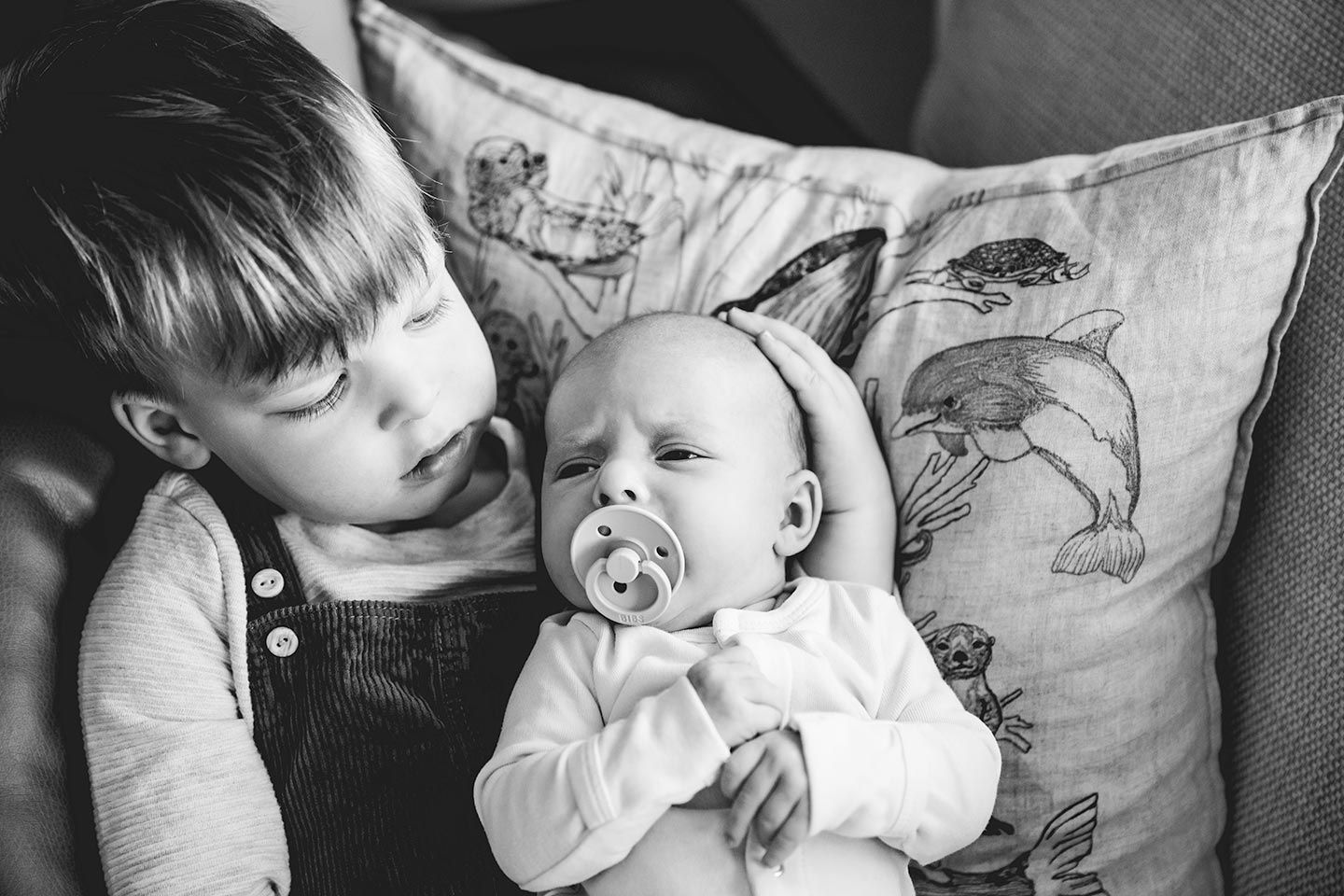 toddler brother holding newborn baby sister on the couch during their in-home newborn photo session