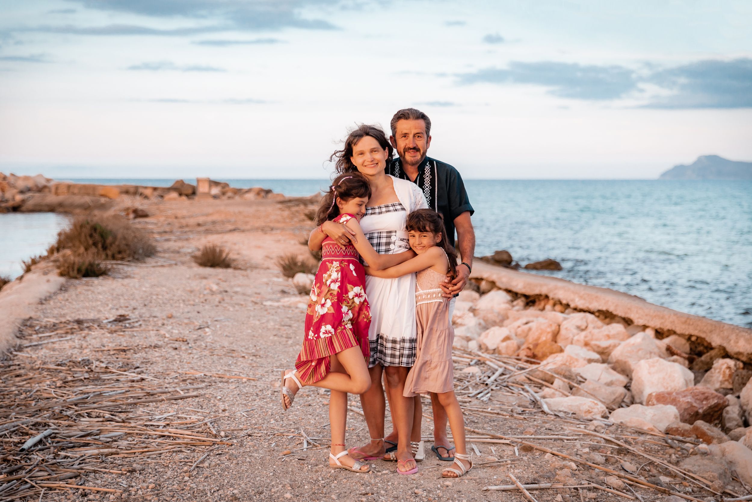 A happy family posing together on a scenic coastal path by the sea during a lifestyle session in Mallorca.