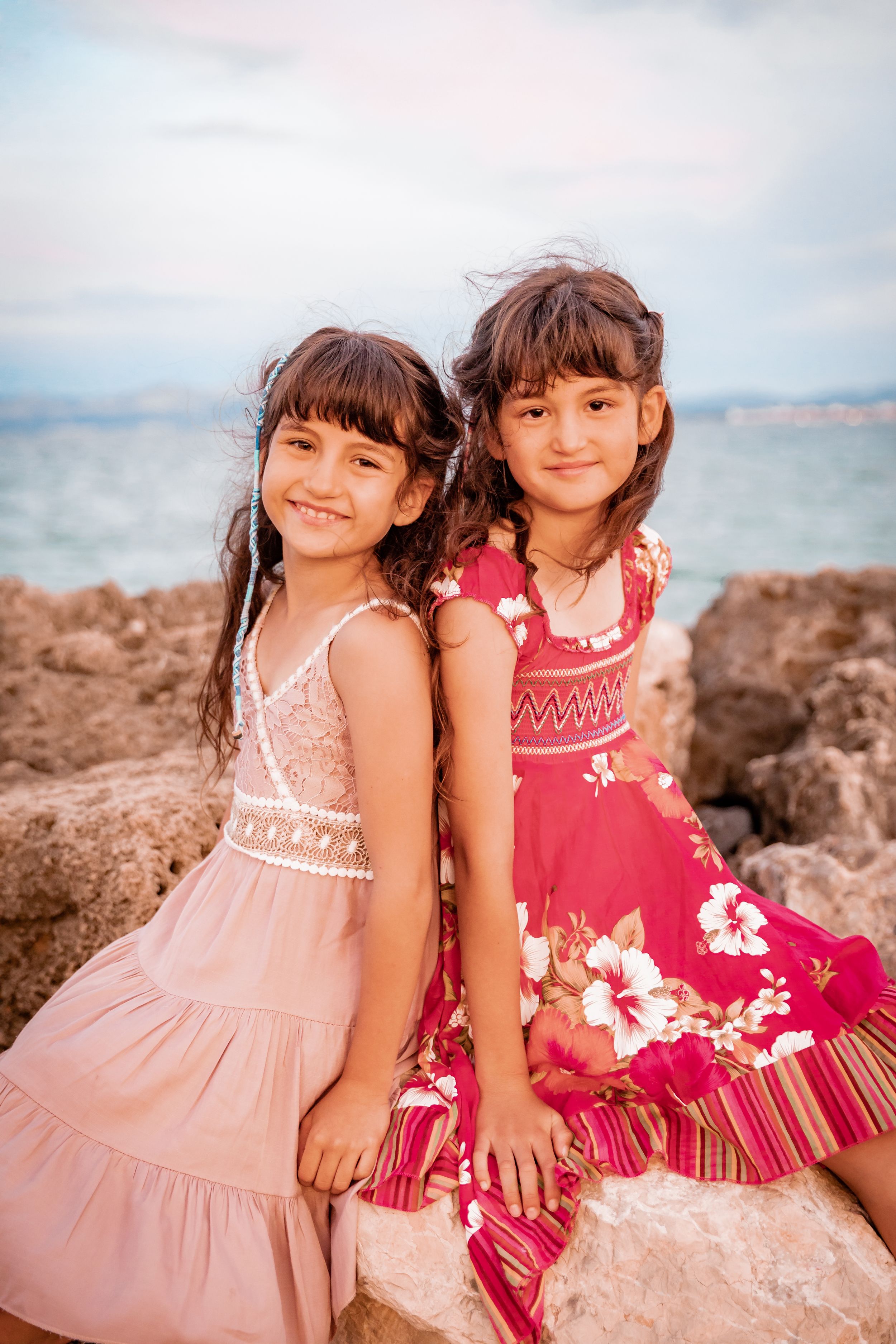 Two young sisters posing back-to-back on coastal rocks during a lifestyle family vacation shoot in Mallorca.