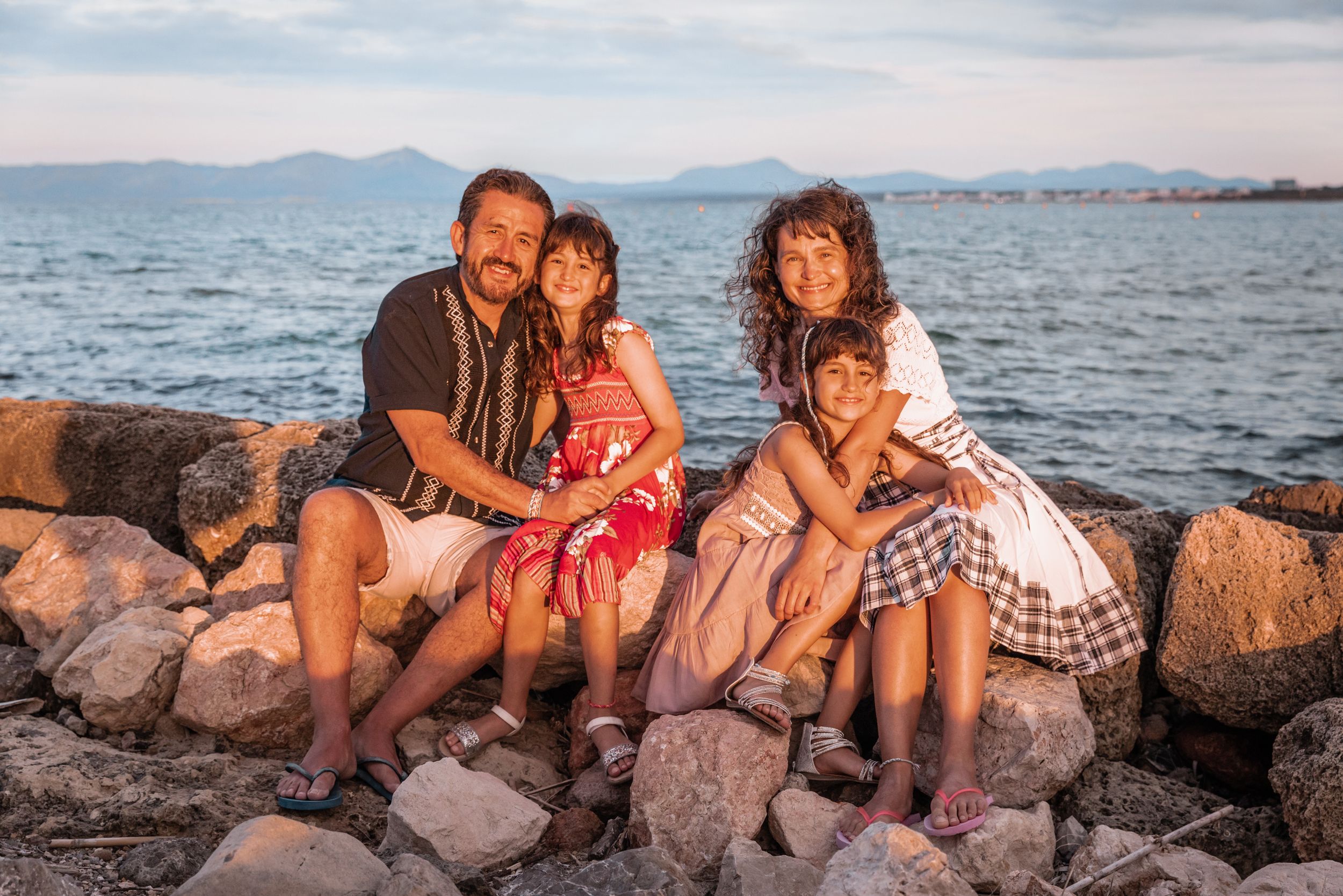 A beautiful family moment all sitting together on a rocky coastal path by the sea during a lifestyle session in Mallorca.